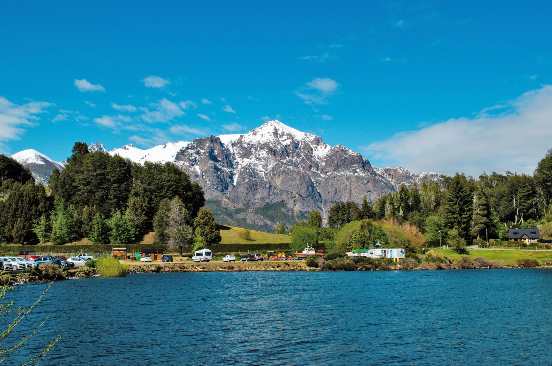 Lago y montañas nevadas en Bariloche con un bosque en primer plano.