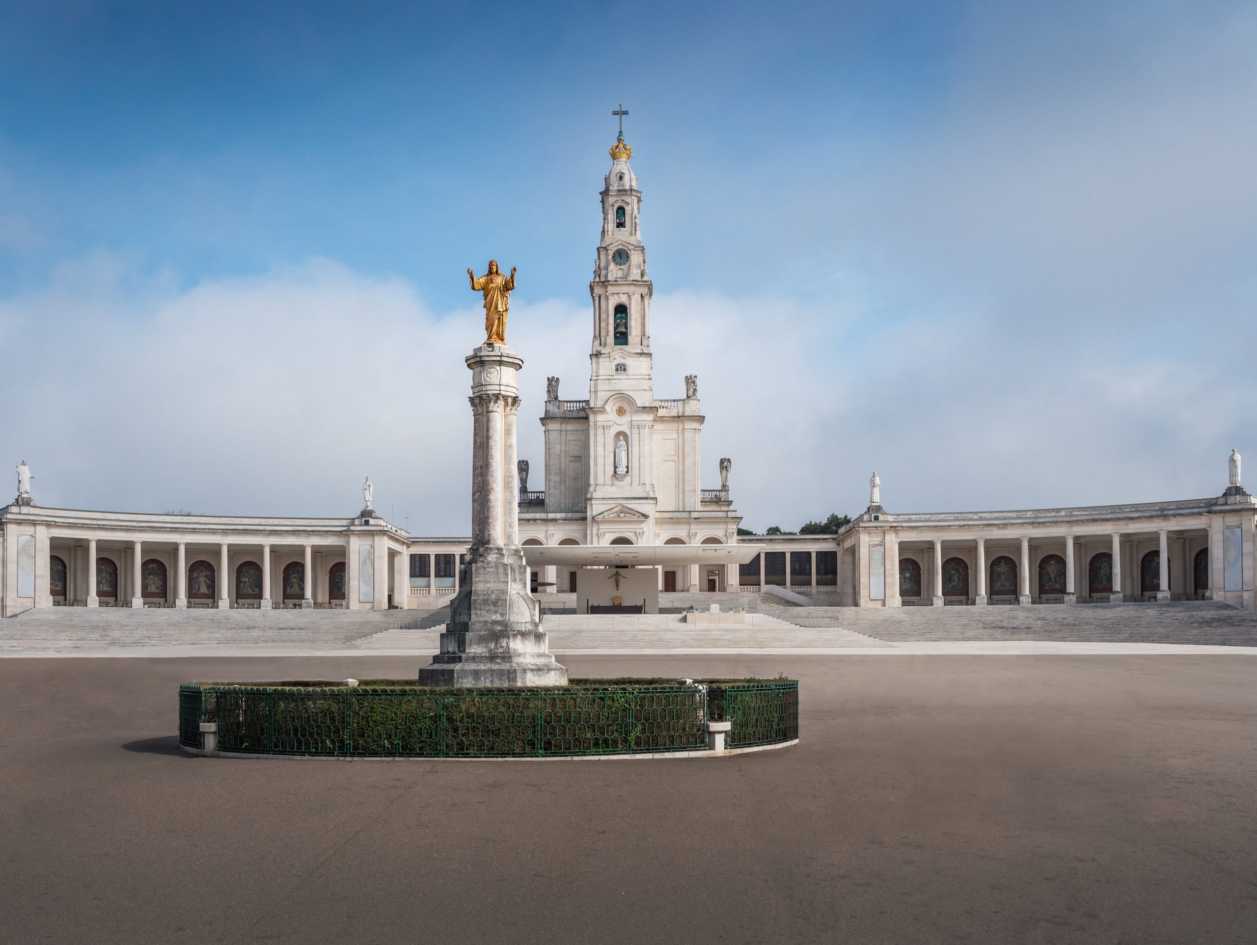 Vista frontal del Santuario de Nuestra Señora del Rosario de Fátima en Portugal, con la estatua dorada del Sagrado Corazón de Jesús en el centro de la gran explanada.
