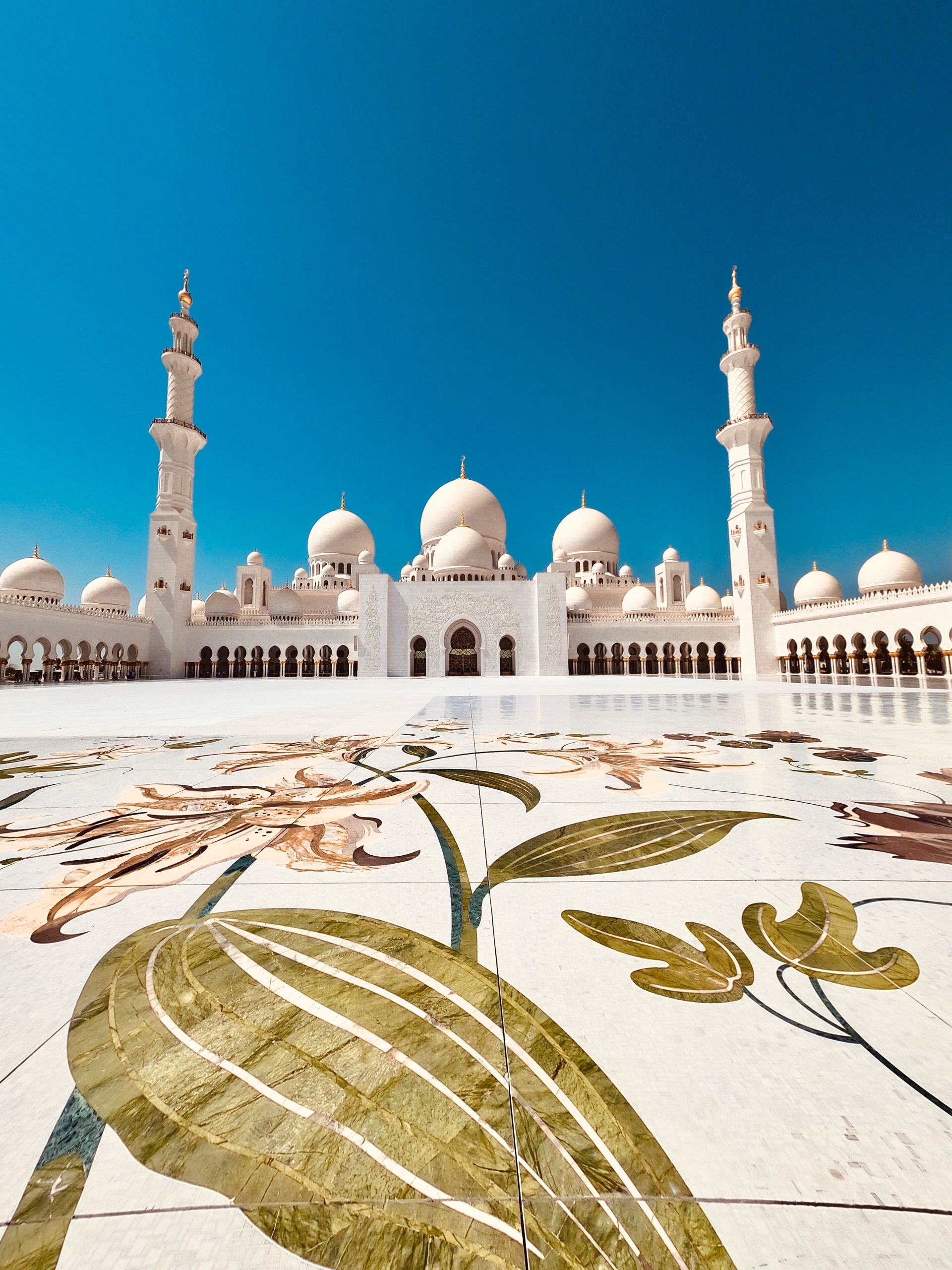 Vista de los minaretes y cúpulas blancas de la Gran Mezquita Sheikh Zayed en Abu Dabi, con detalle de mármol floral en el piso, visita incluida en el tour de quinceañeras con extensión a Dubái